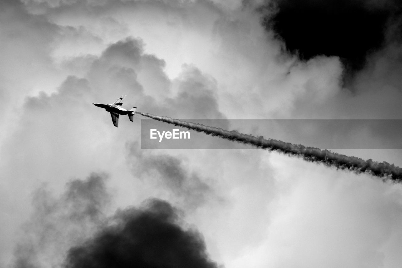 Silhouette aerobatic jet airplane flying between clouds with white smoke