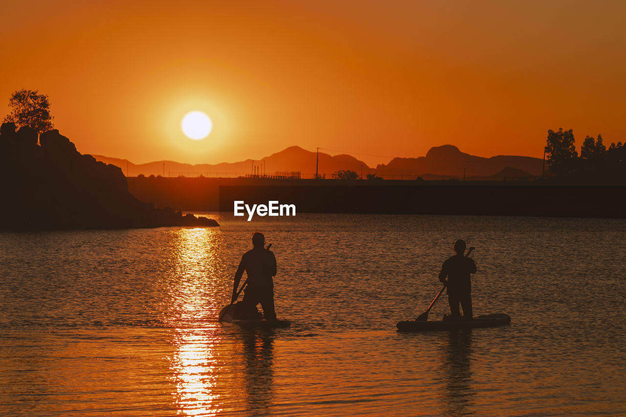 SILHOUETTE MEN BY SEA AGAINST ORANGE SKY