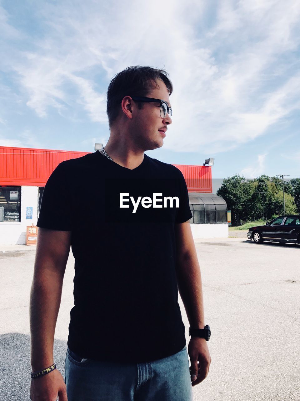 Young man looking away while standing on street against sky