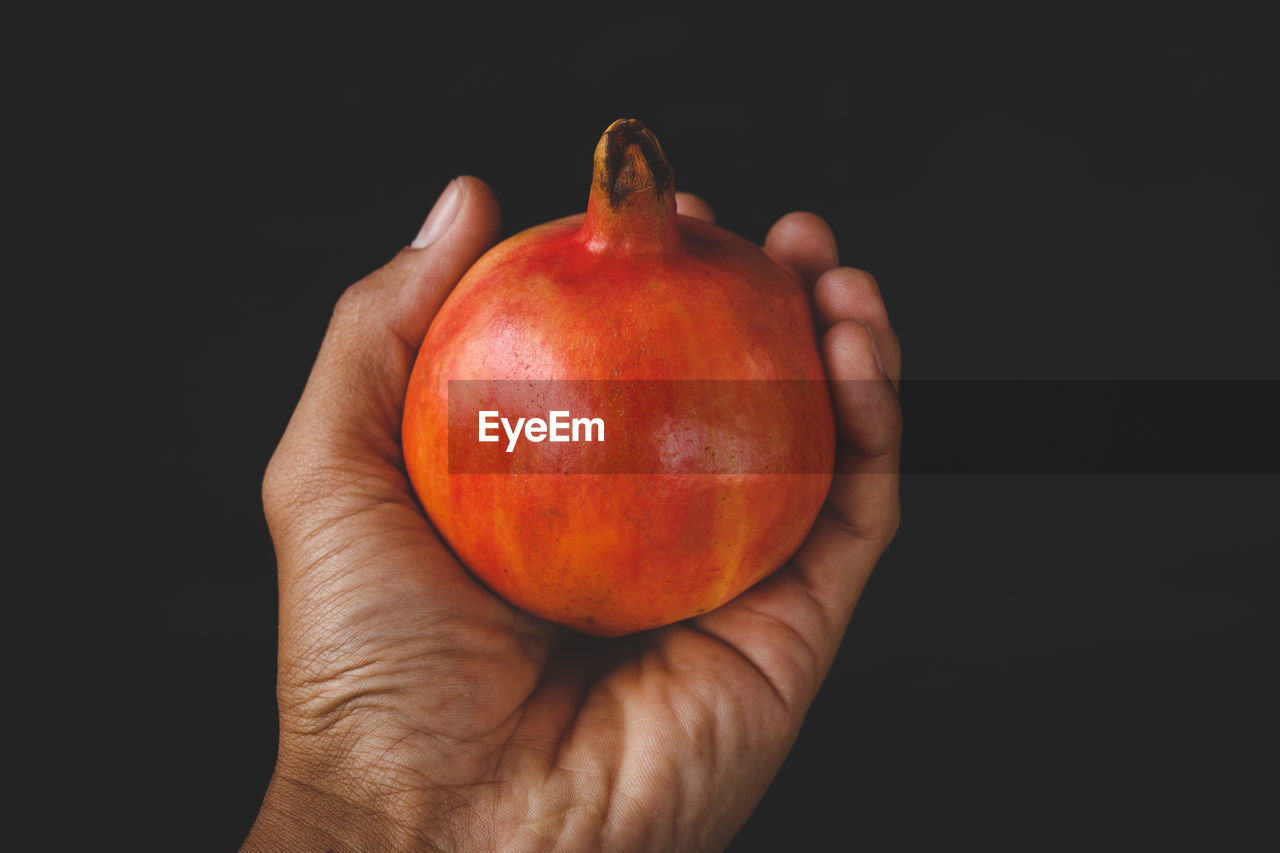 Cropped hand of woman holding pomegranate against black background