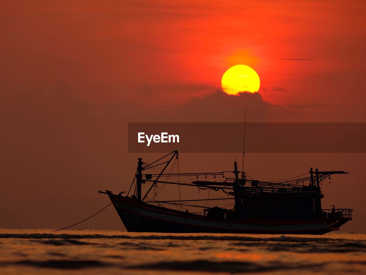 Silhouette boat moored on sea against orange sky