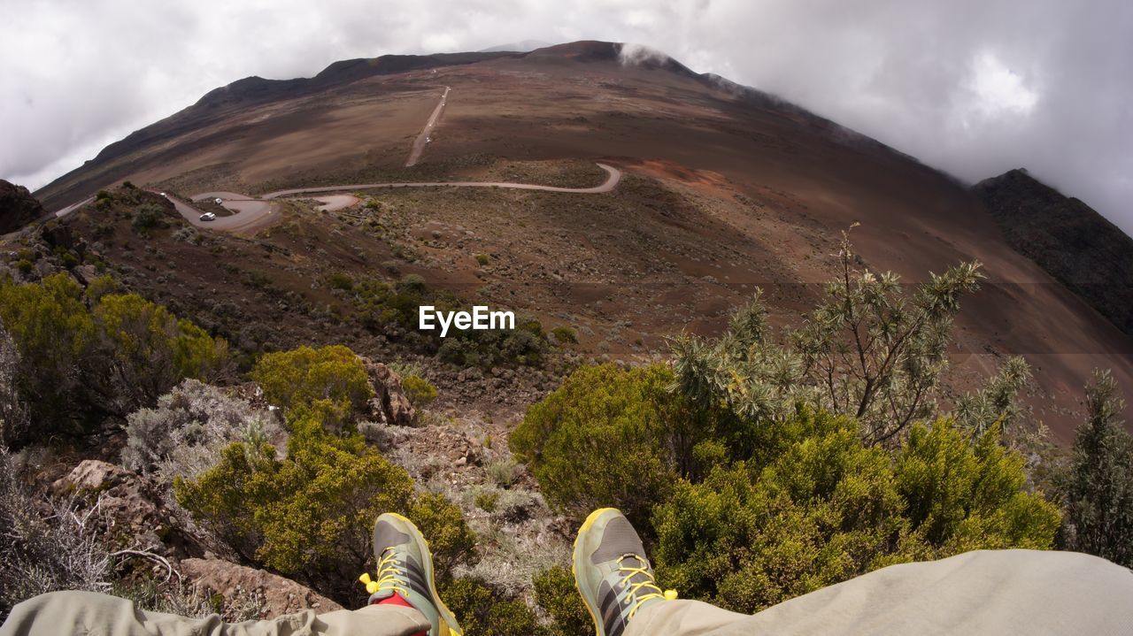 LOW SECTION OF PERSON ON MOUNTAIN LANDSCAPE AGAINST SKY