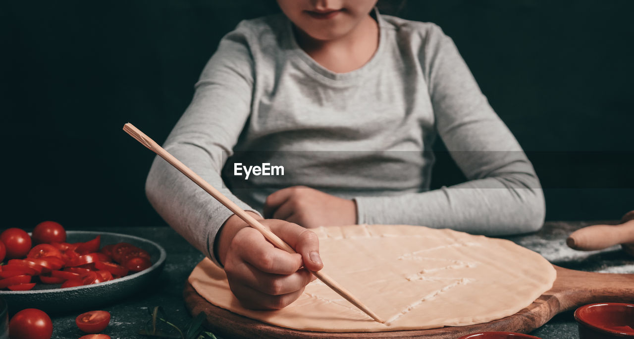 A child's hand draws a christmas tree with a wooden stick on pizza dough