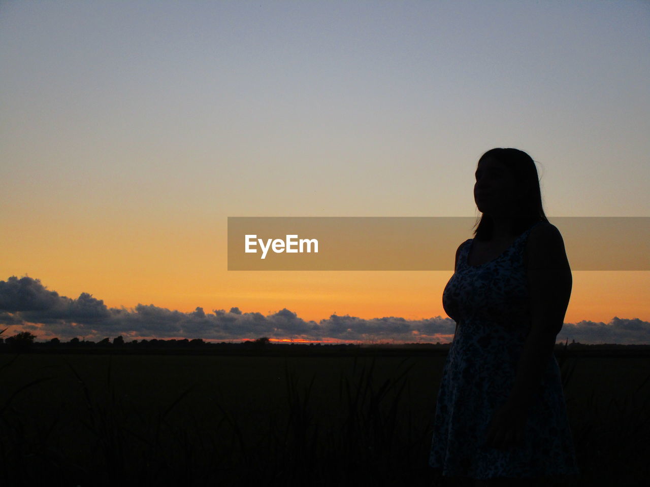 Silhouette teenage girl standing on field against sky during sunset