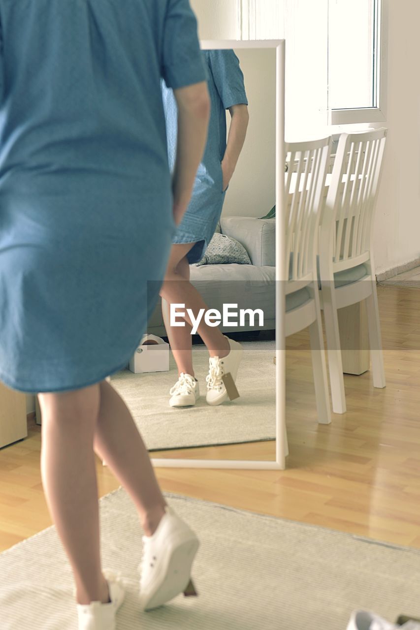 LOW SECTION OF WOMAN STANDING ON WOODEN FLOOR