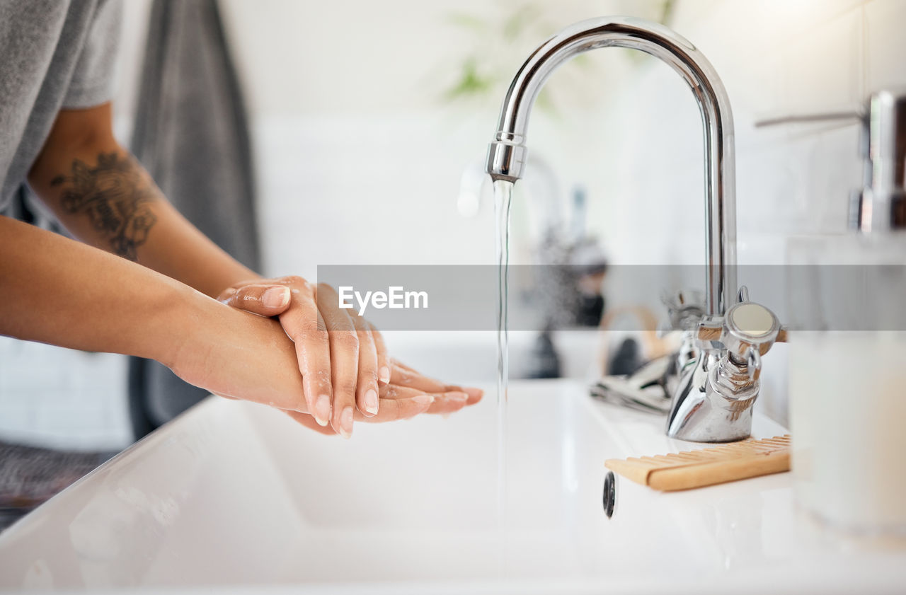 cropped hand of man washing hands in sink