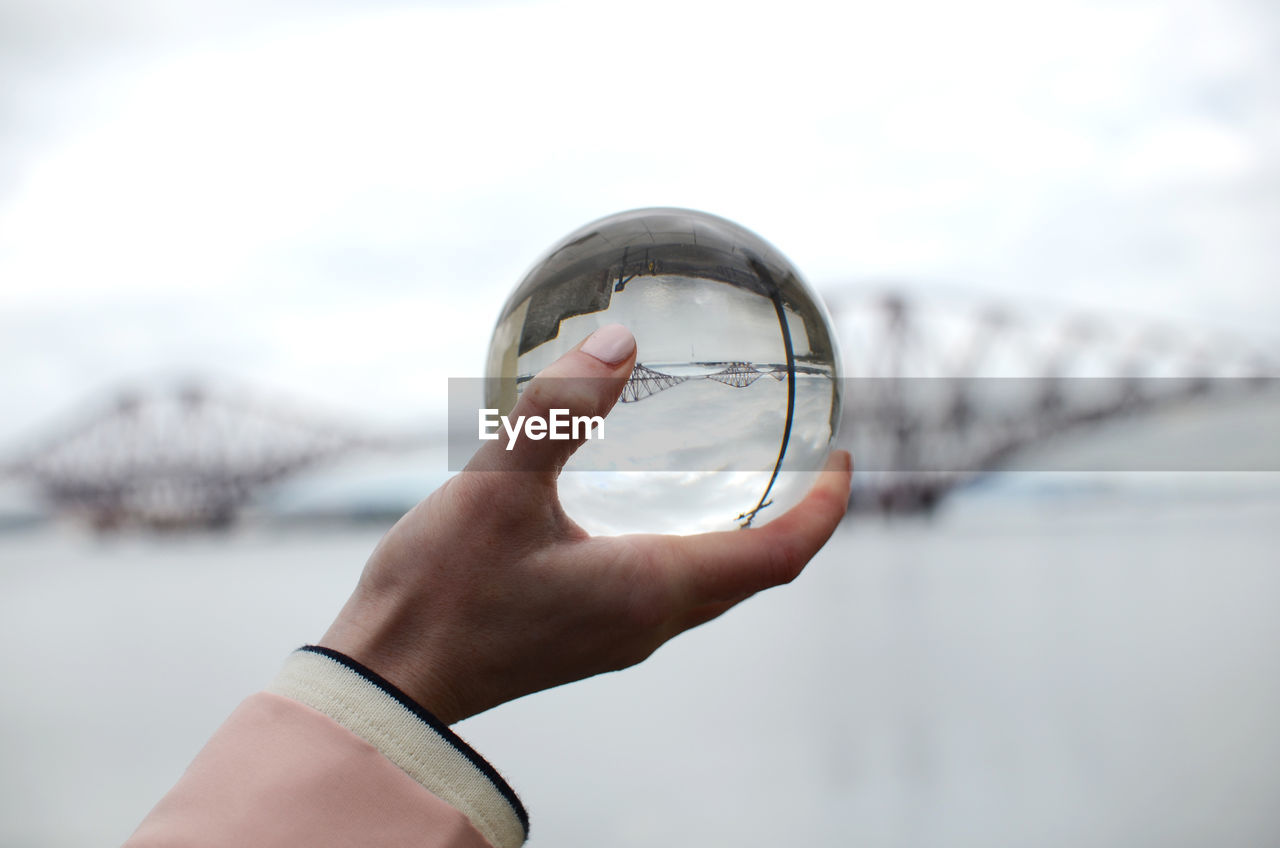 Cropped hand of woman holding crystal ball against bridge in city