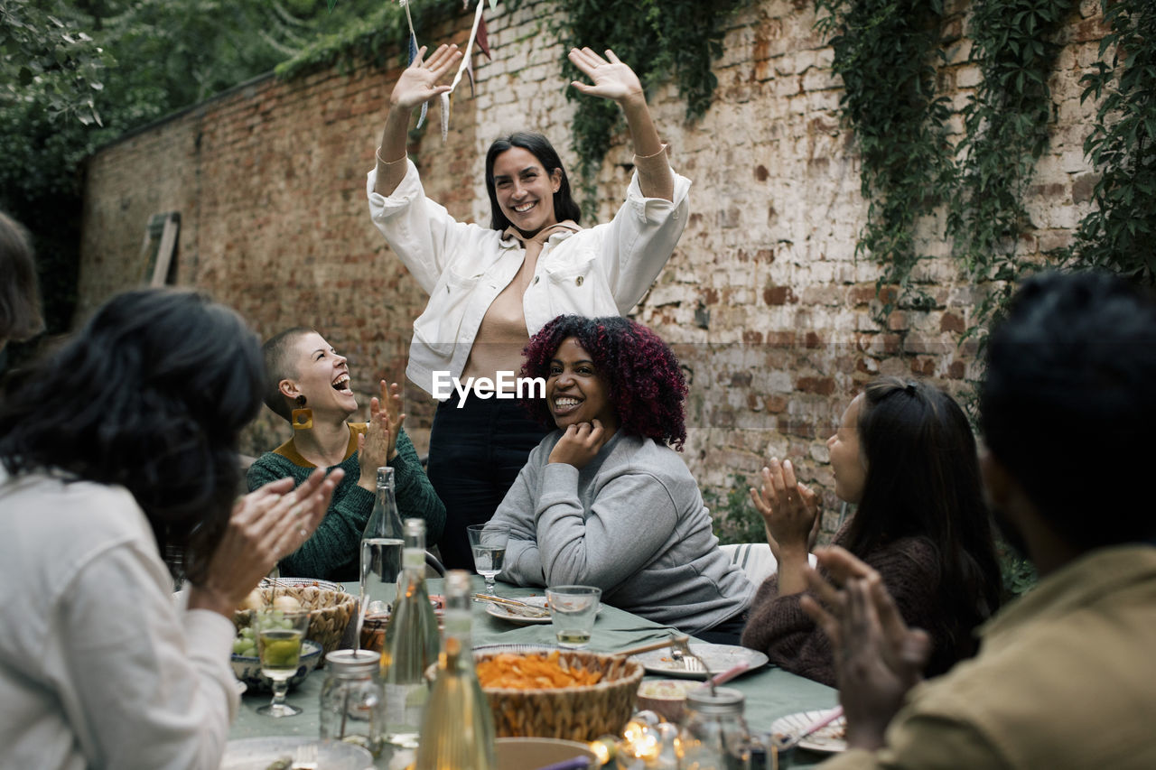 Smiling woman gesturing while enjoying with friends during dinner party in back yard