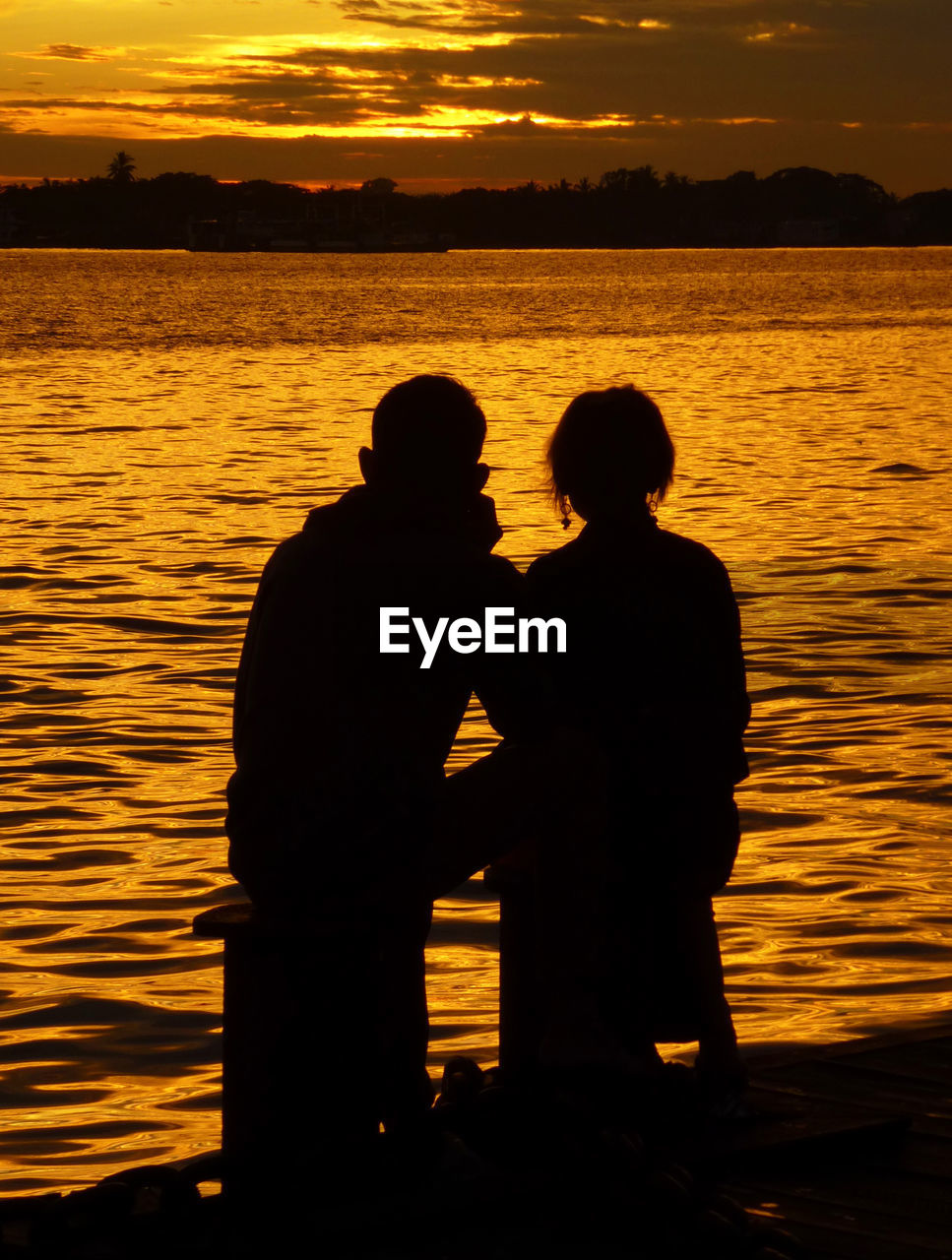 Silhouette couple standing against sea during sunset