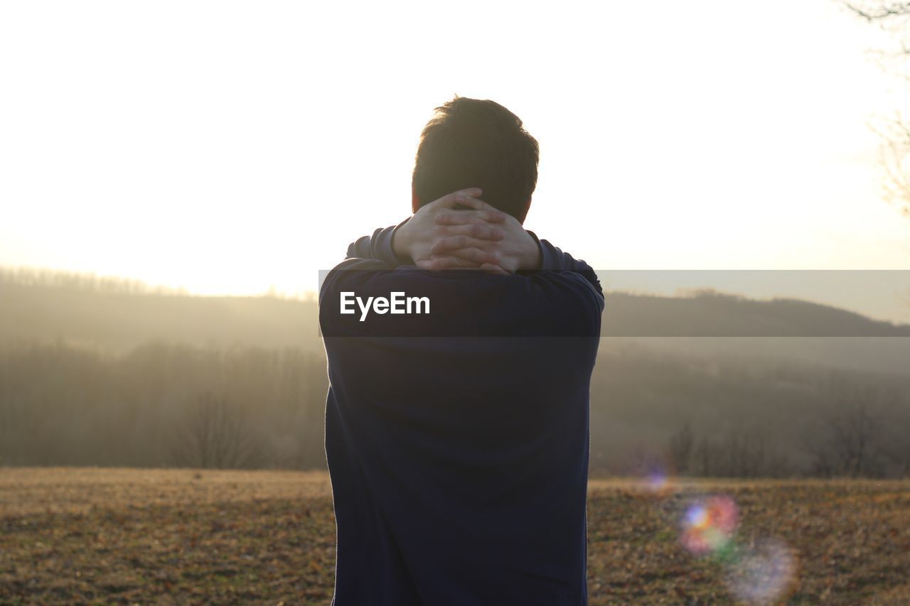 Rear view of man standing on field against sky during sunset