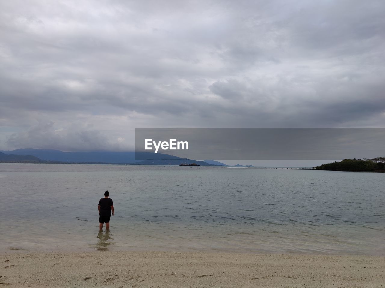 rear view of woman walking at beach against cloudy sky