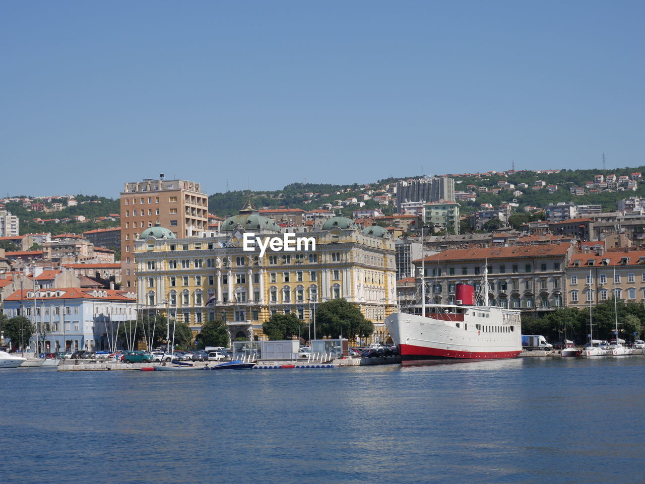 Sailboats in sea by buildings against clear sky