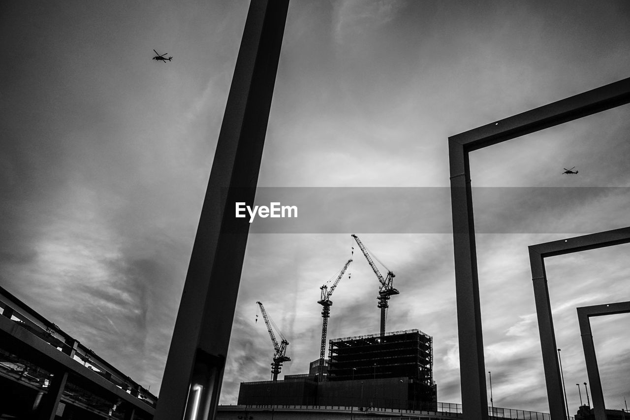 LOW ANGLE VIEW OF CRANES AGAINST BUILDINGS