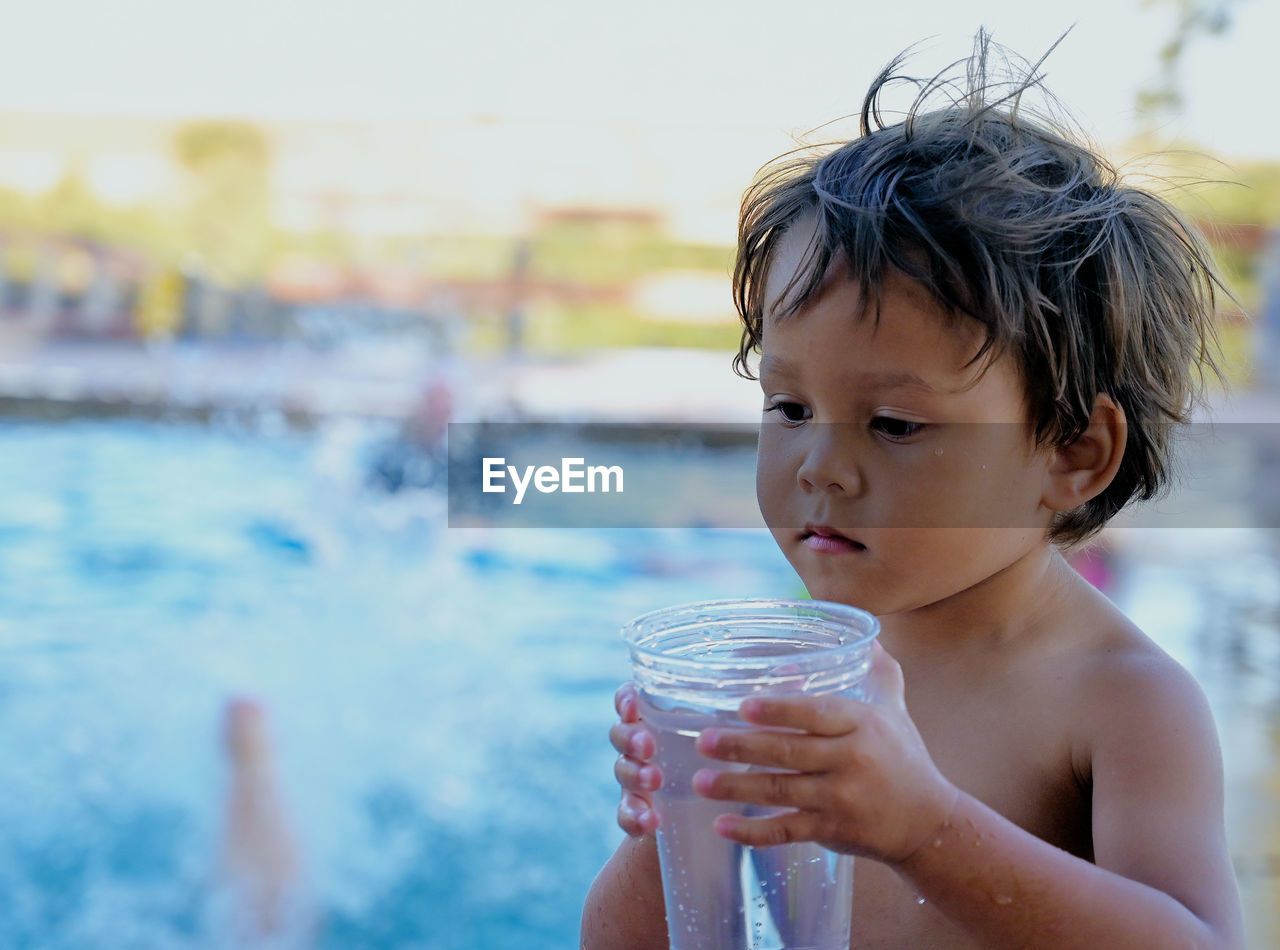 Shirtless boy holding drinking glass by swimming pool