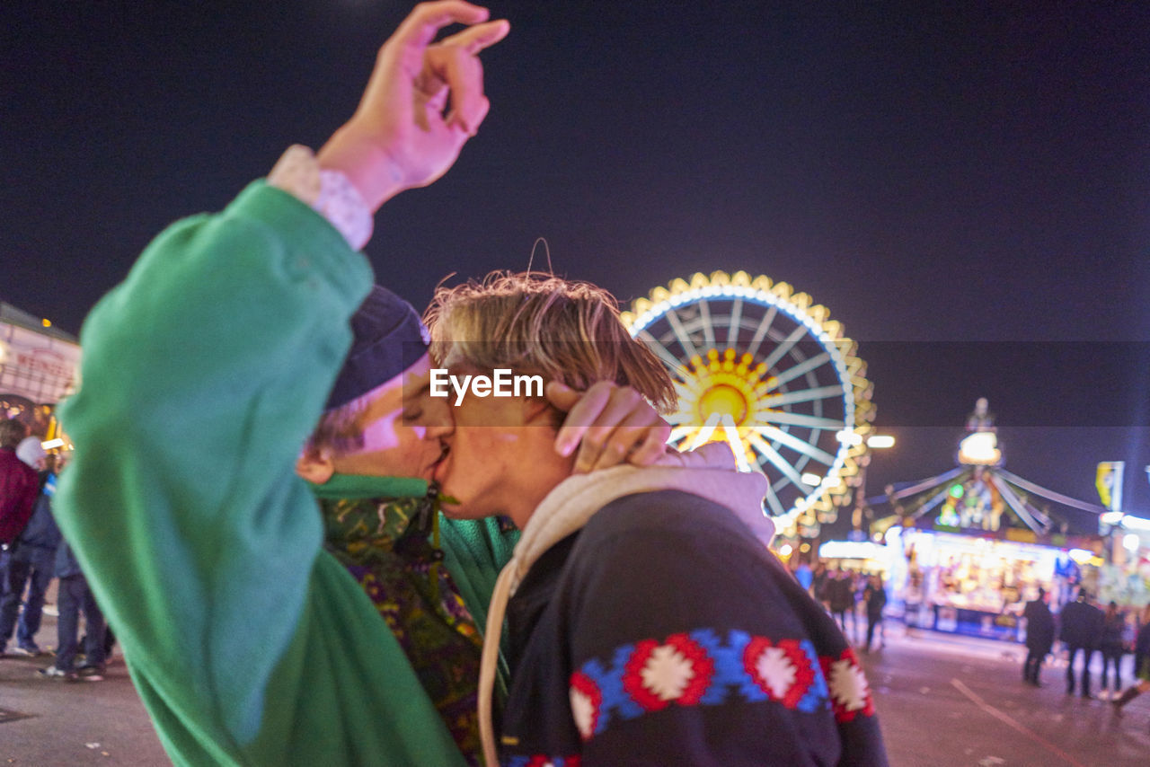 Gay men kissing at amusement park during night