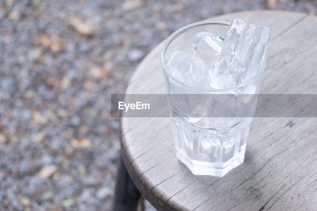 glass, drinking glass, refreshment, drink, household equipment, food and drink, drinking water, water, high angle view, no people, nature, table, day, focus on foreground, wood, cold temperature, cold drink, outdoors, close-up, ice cube, frozen, still life, freshness, transparent