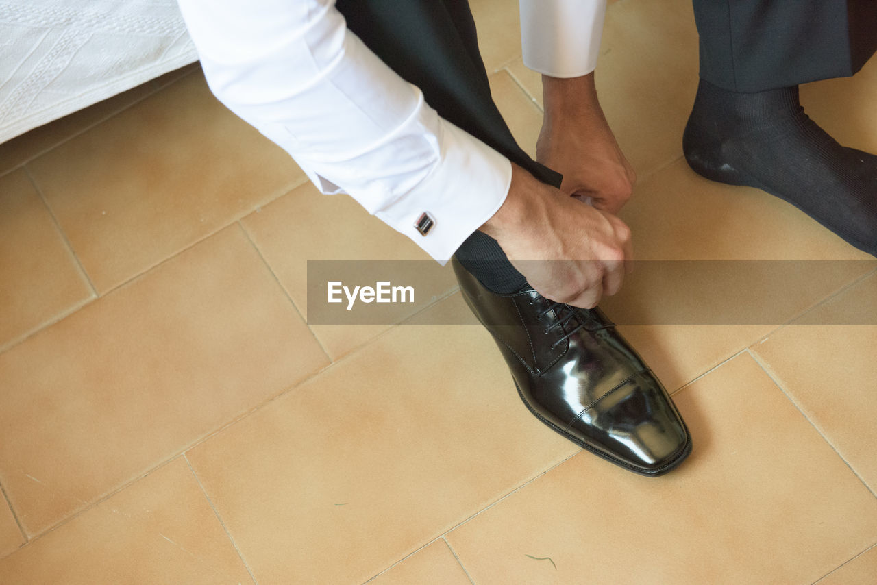 Low section of man tying shoelace on floor at home