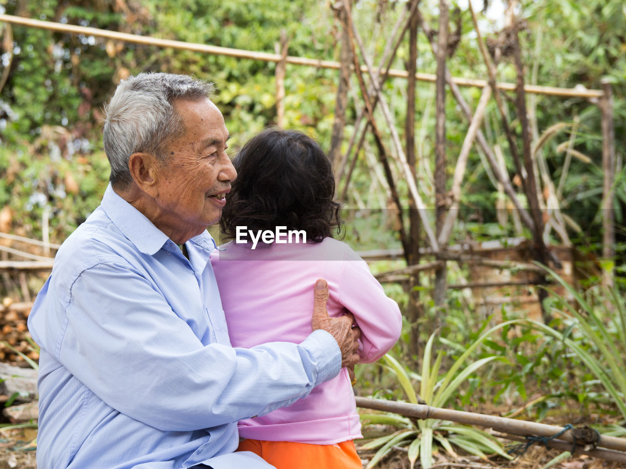 Side view of senior man holding granddaughter in yard 