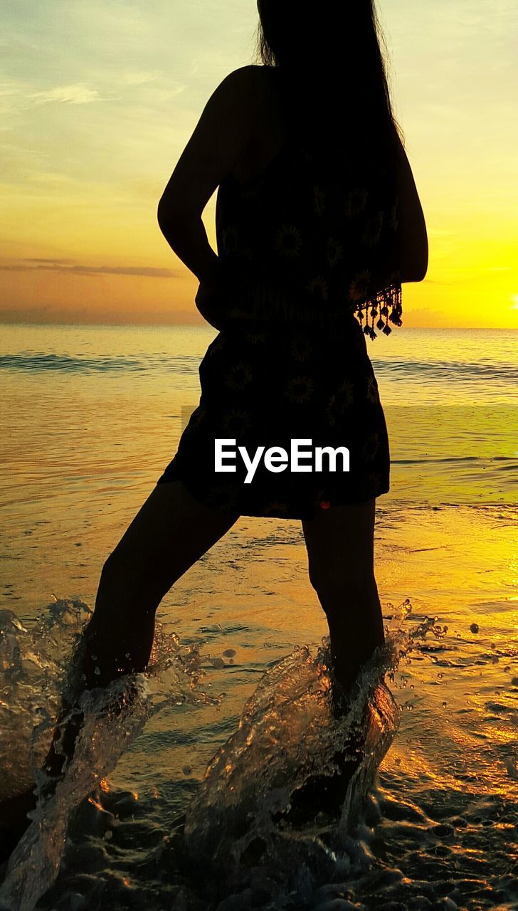 Silhouette woman with long hair standing on beach during sunset