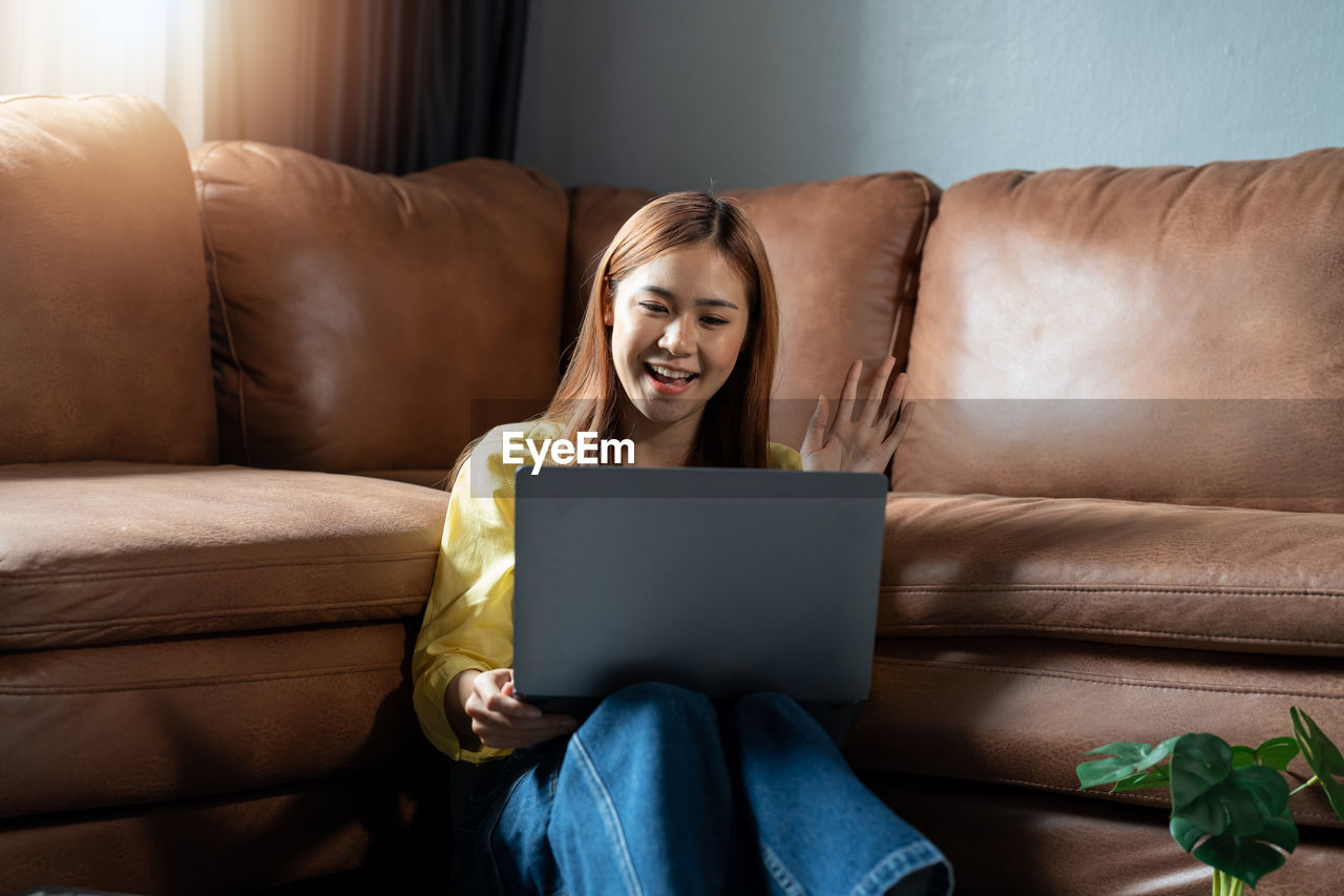young woman using laptop while sitting on sofa at home