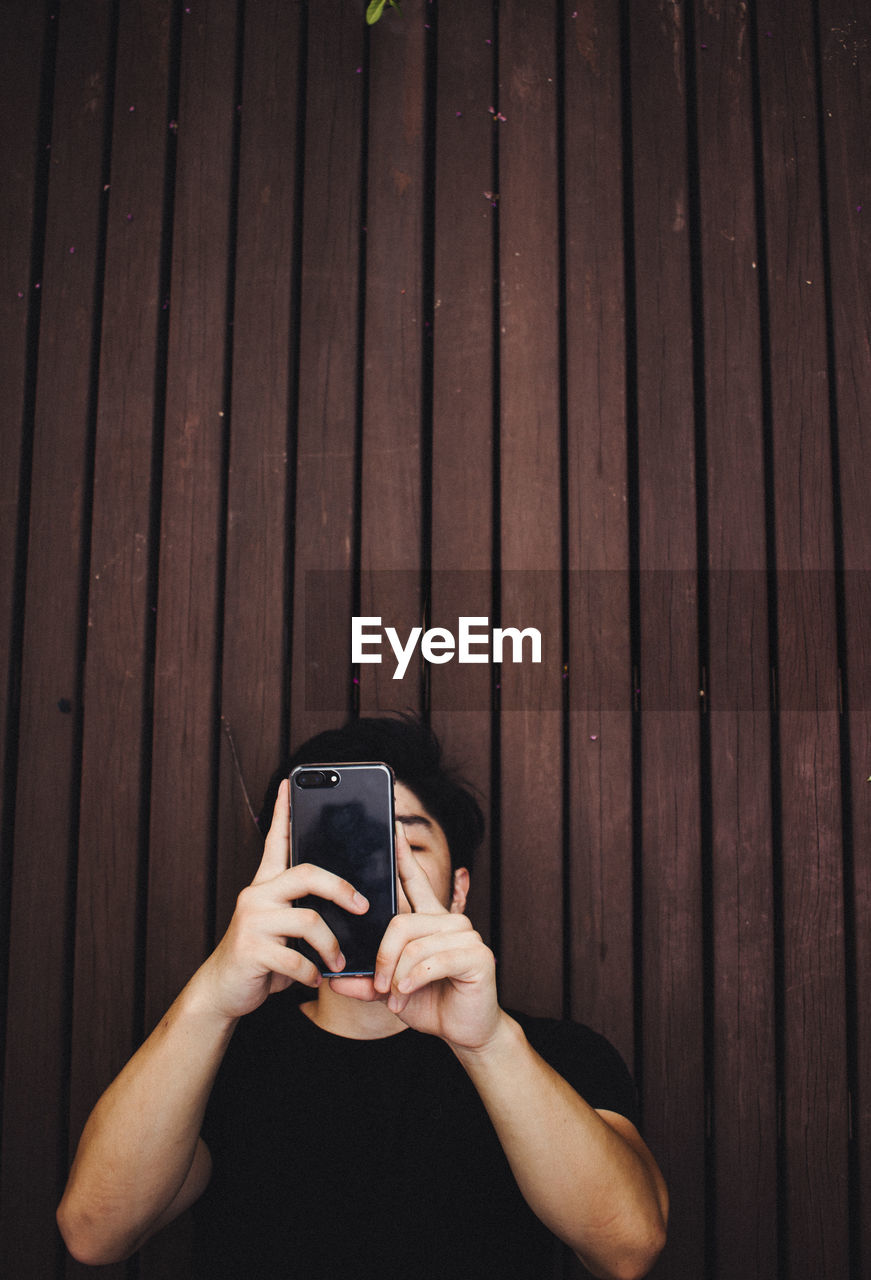 Young man using mobile phone while standing by wall