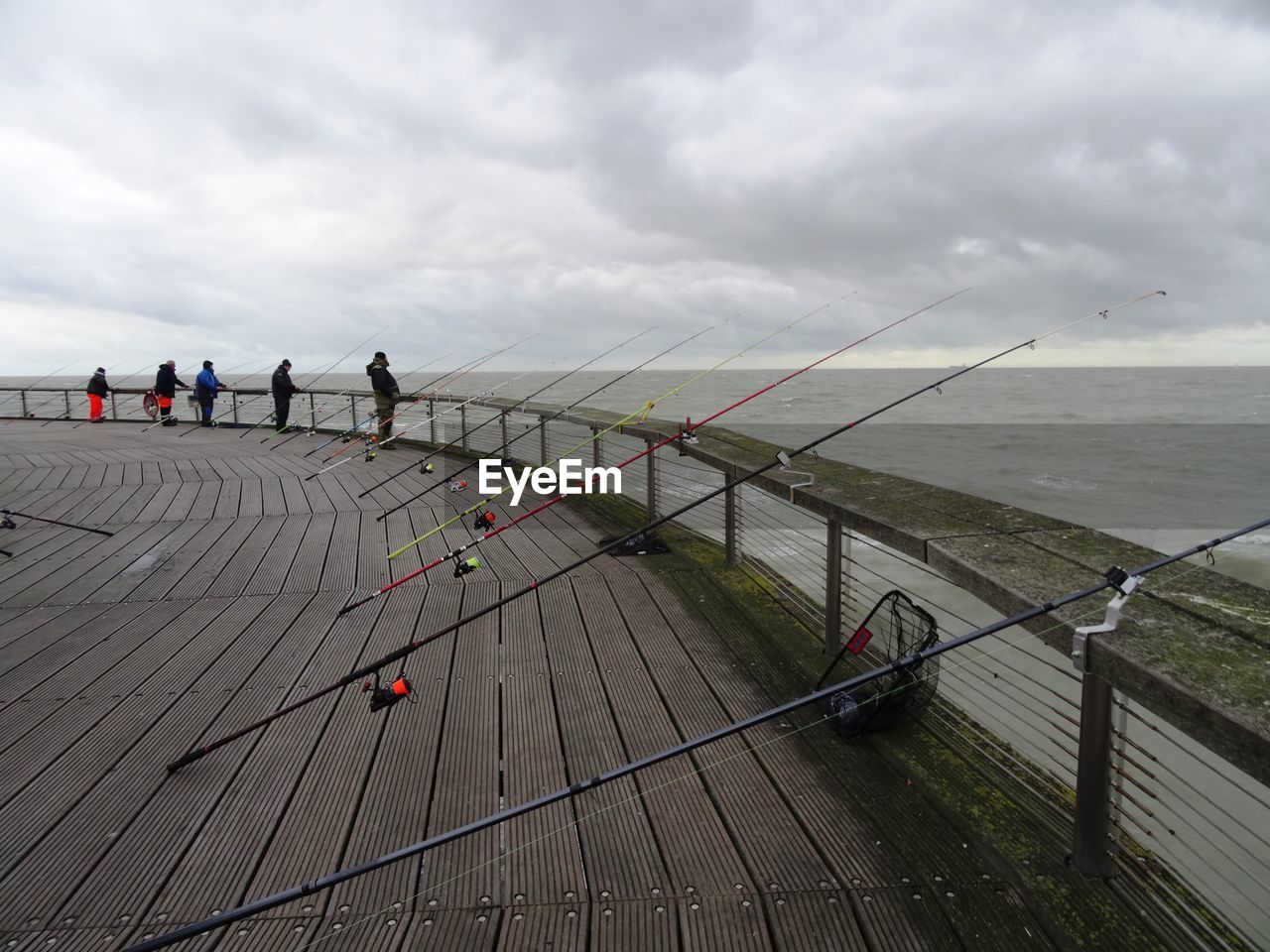 People fishing at sea against cloudy sky