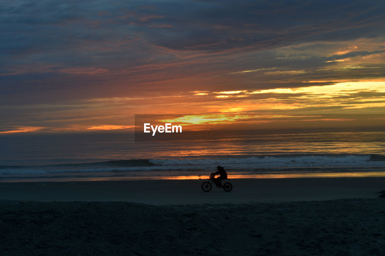MAN RIDING BICYCLE ON BEACH DURING SUNSET