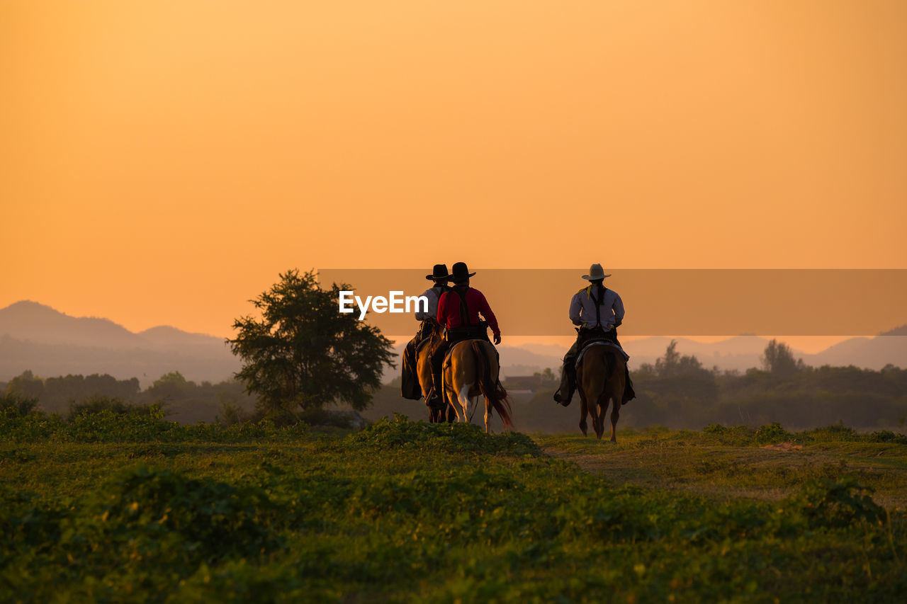 People riding horse on field against sky during sunset