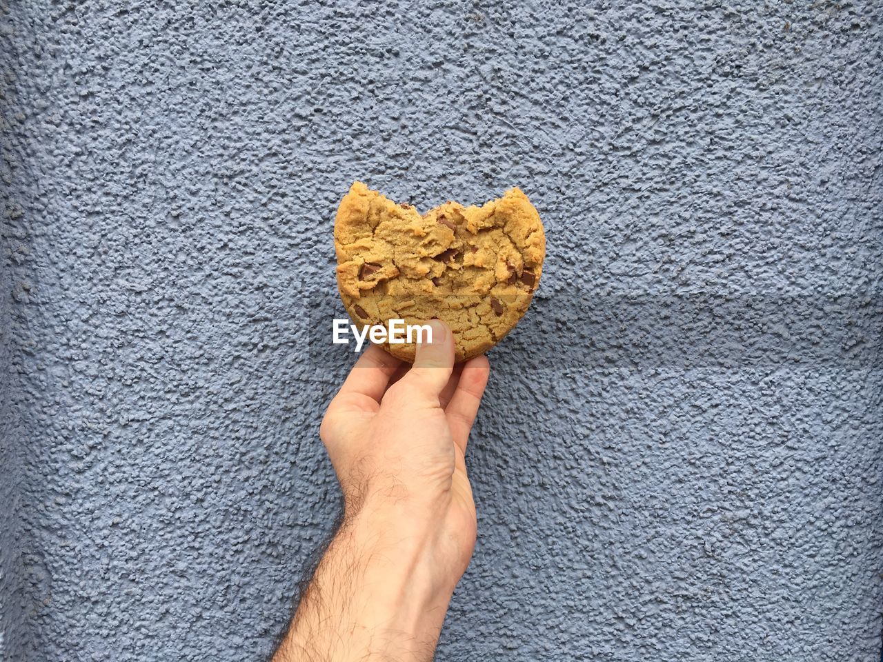 Cropped image of man holding cookie against wall