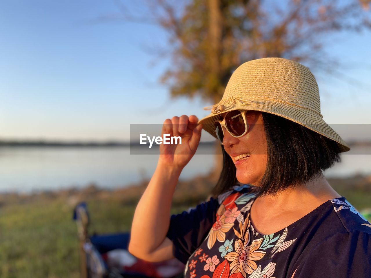 Smiling mature woman wearing hat standing outdoors during sunset