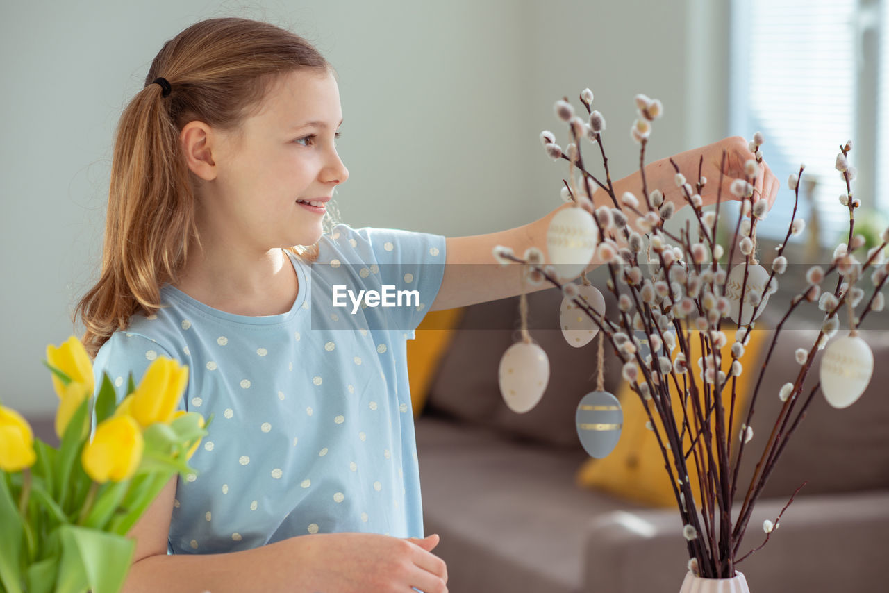 flower, spring, women, child, one person, flowering plant, plant, indoors, childhood, yellow, female, lifestyles, floristry, nature, smiling, emotion, home interior, adult, happiness, domestic life, holding, casual clothing, looking, flower arrangement, hairstyle, bouquet, growth, waist up, portrait, domestic room, standing, blond hair, cute