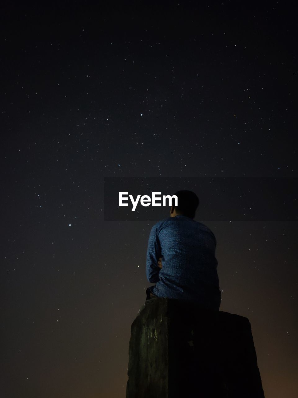 Low angle view of man sitting on rock against star field at night