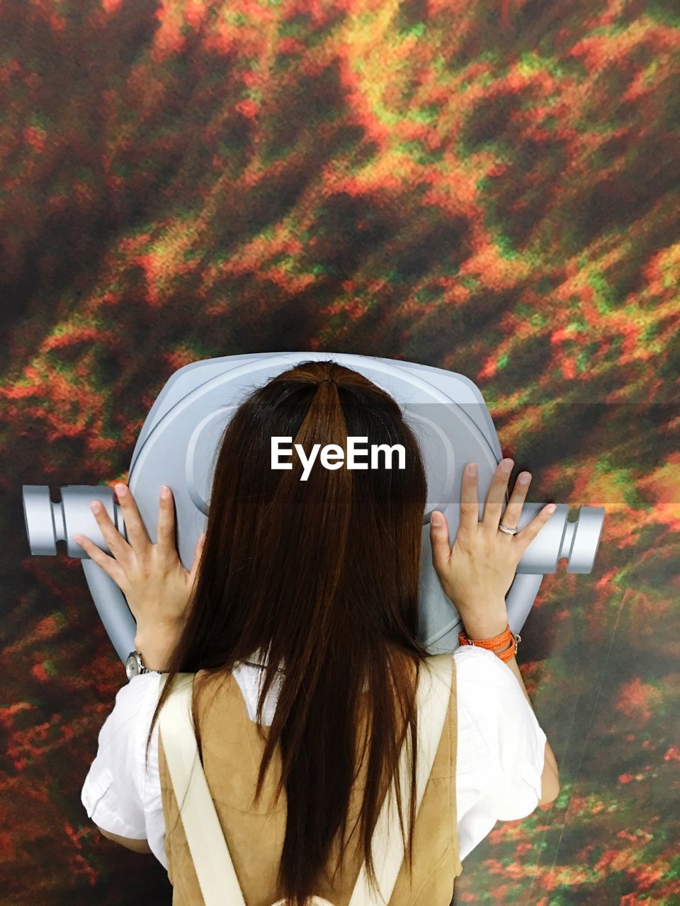 Rear view of woman looking through coin-operated binoculars at sky