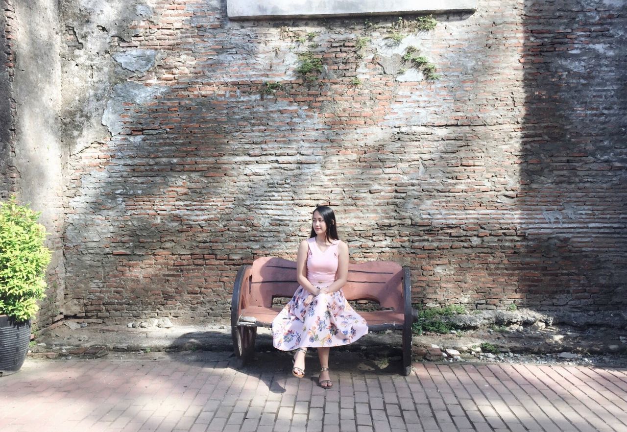 Smiling young woman sitting on bench against wall