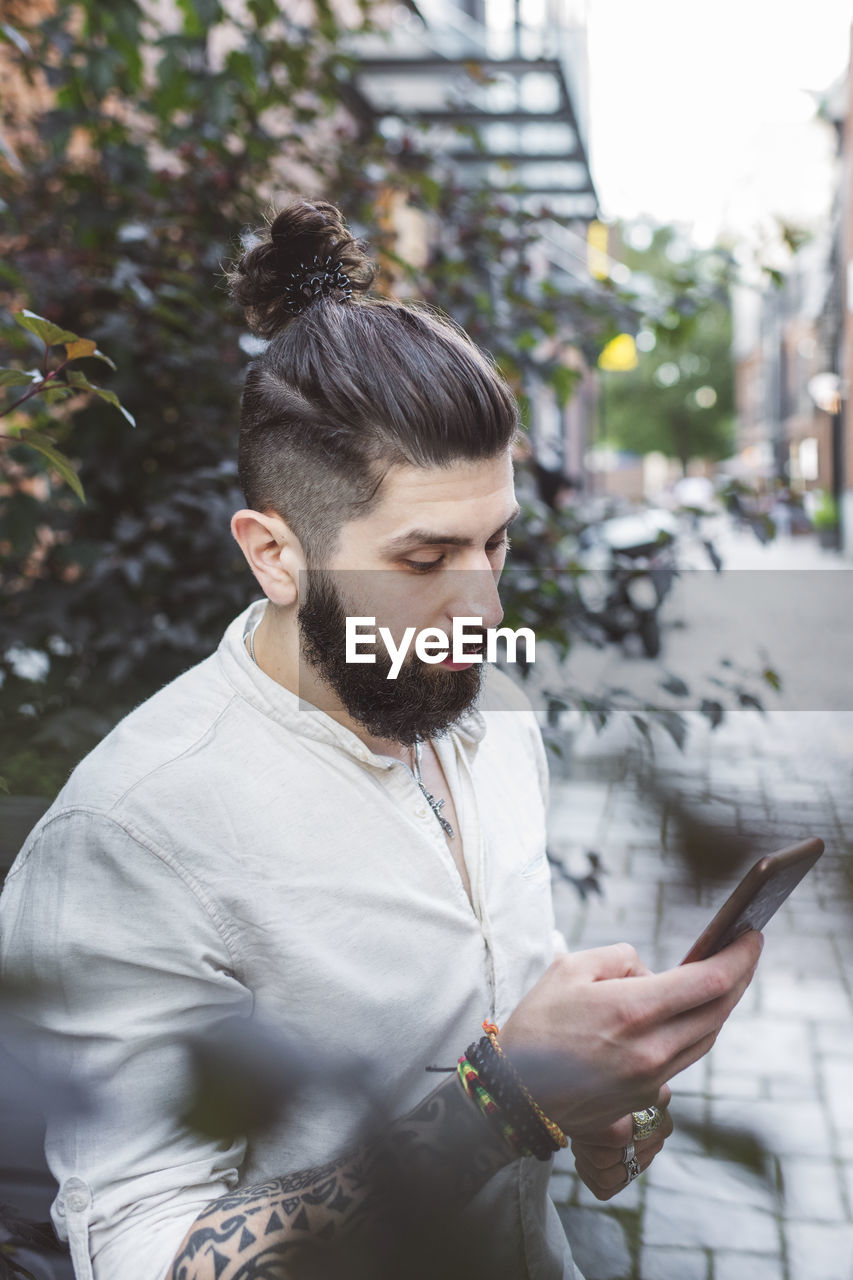 Hipster man using smartphone while standing by plants