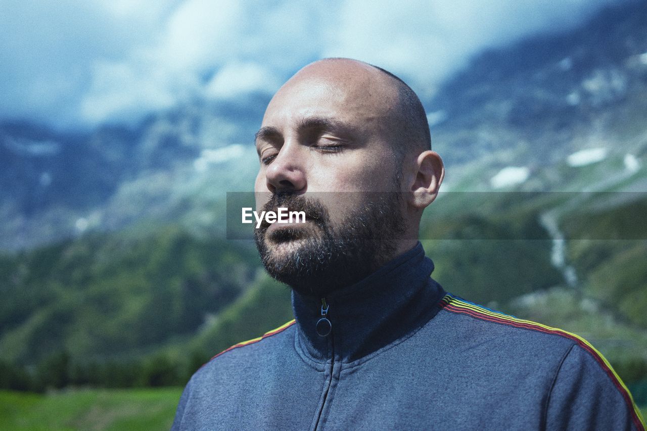 Close-up of man with eyes closed against mountains