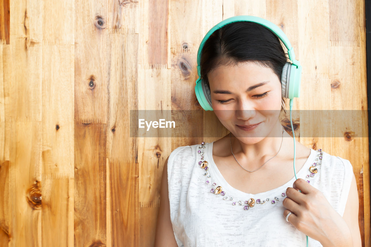 Woman listening to music against wooden wall