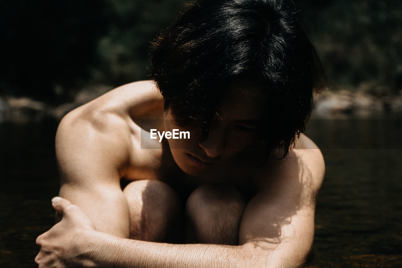 Midsection of shirtless boy sitting in water