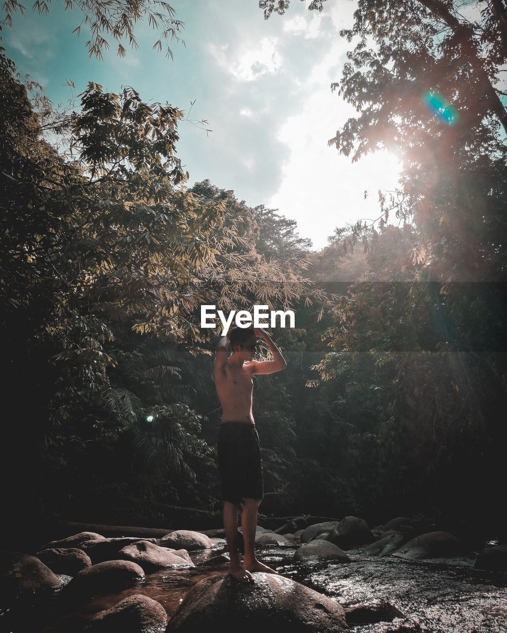 Full length of shirtless young woman standing on rock in forest