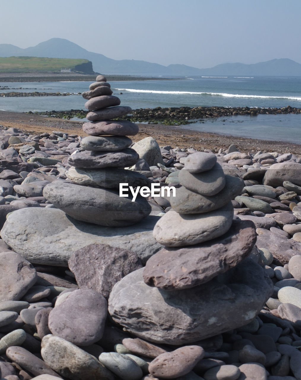 Stacked stones at beach against clear sky during sunny day