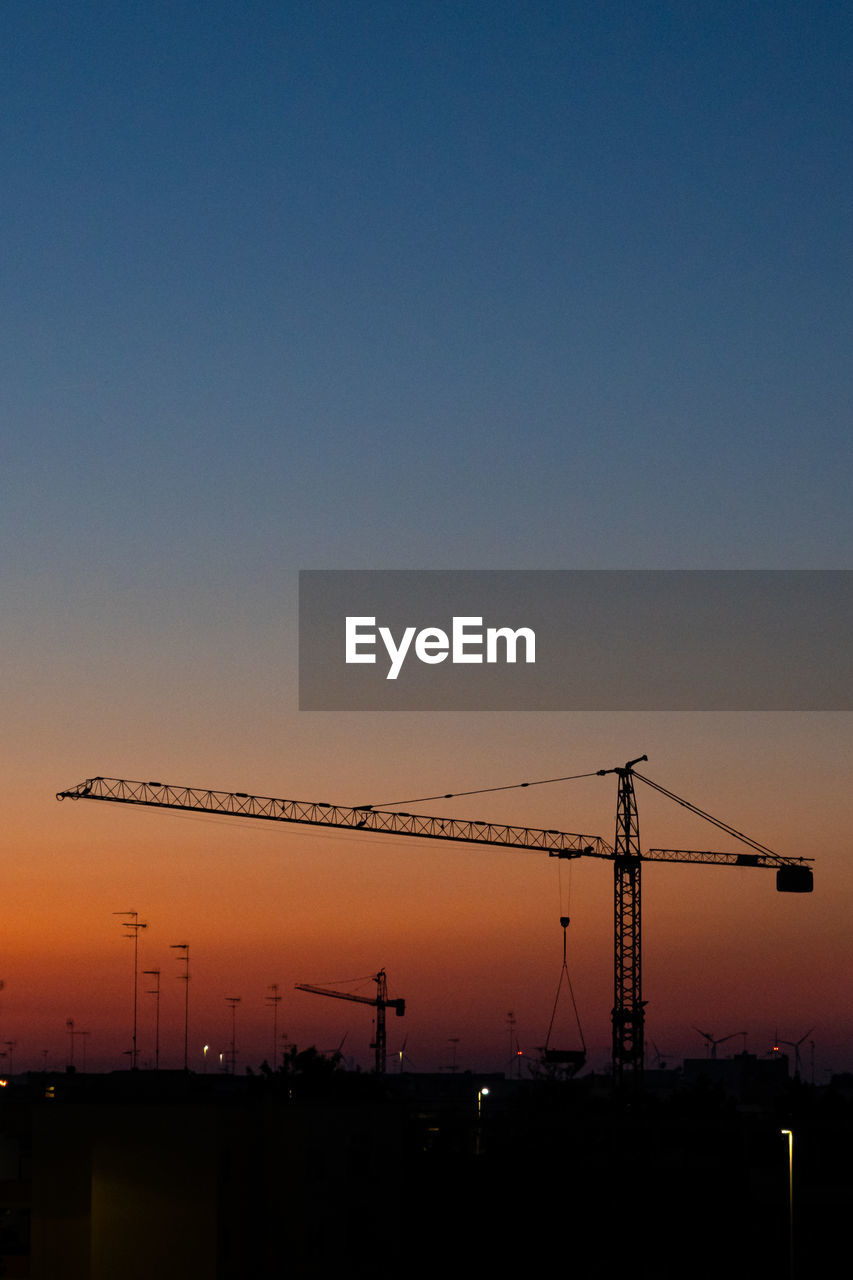 SILHOUETTE CRANES AGAINST CLEAR SKY DURING SUNSET