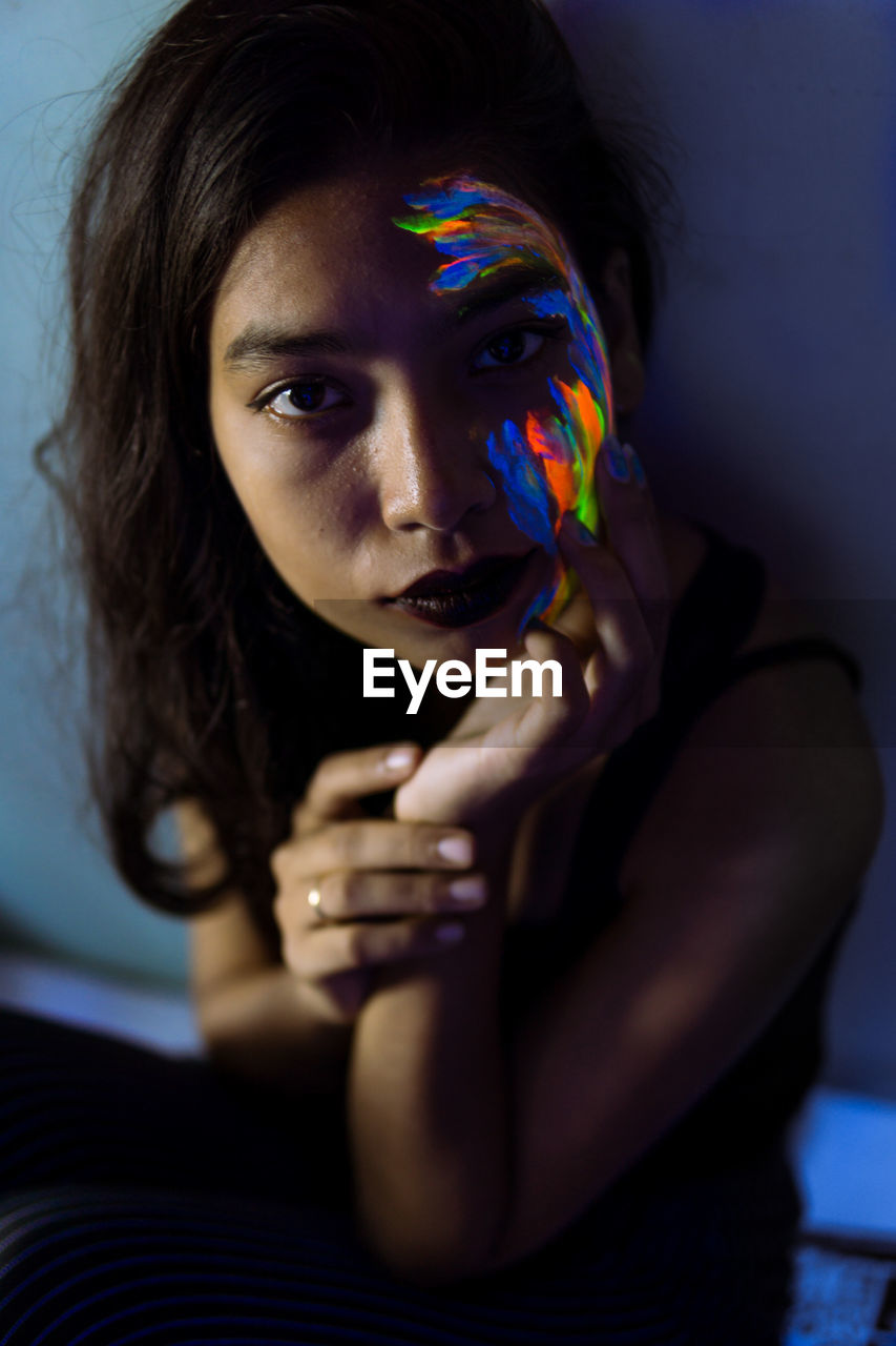 High angle portrait of young woman with face paint sitting in darkroom