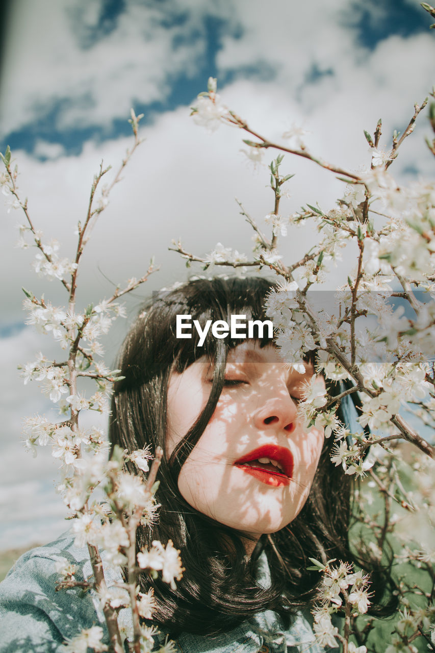 Close-up of woman with eyes closed by plants against sky