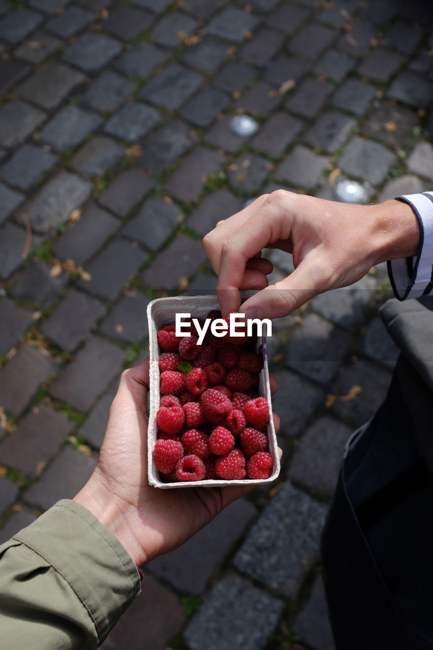 Cropped hand of woman giving raspberry to man on footpath