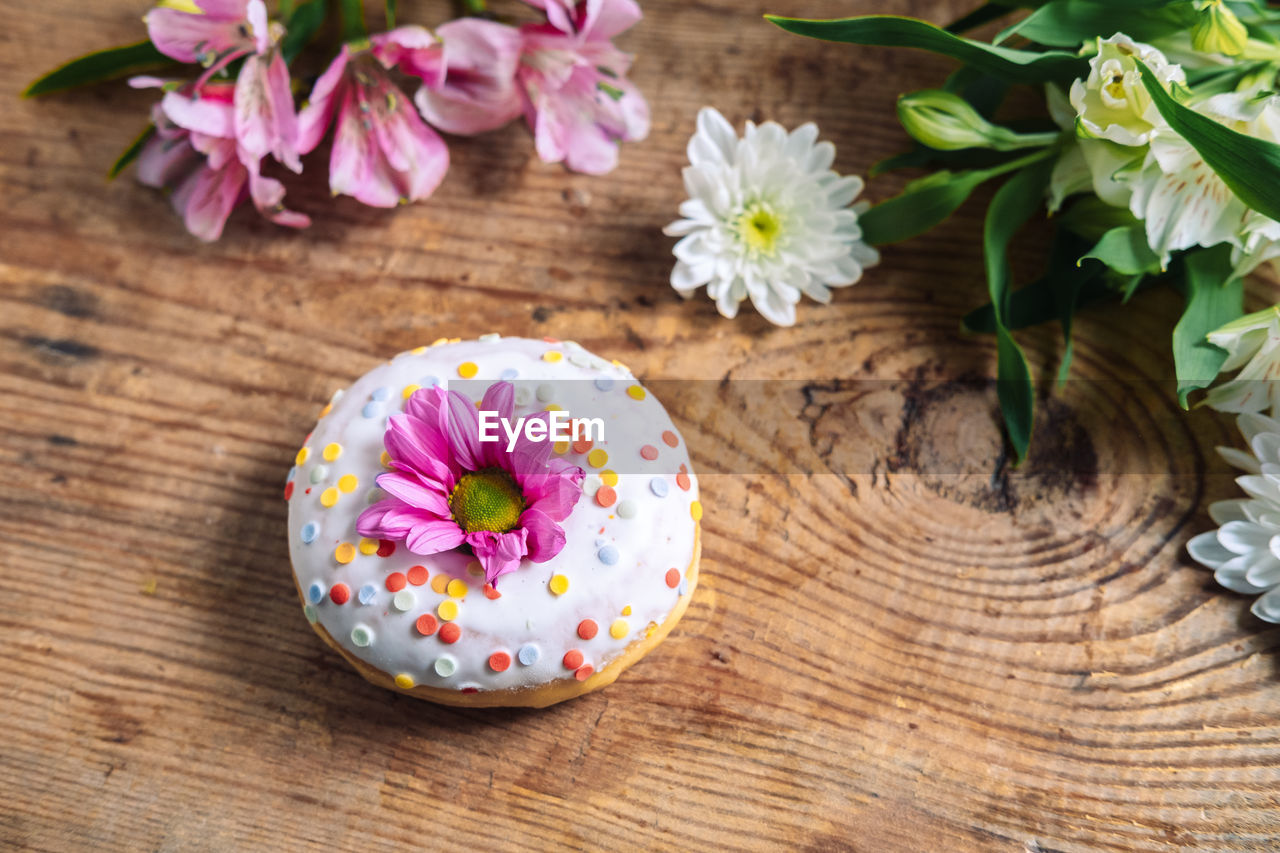 Chamomile bud on top of a donut on a wooden background with a bouquet of alstroemerias. 