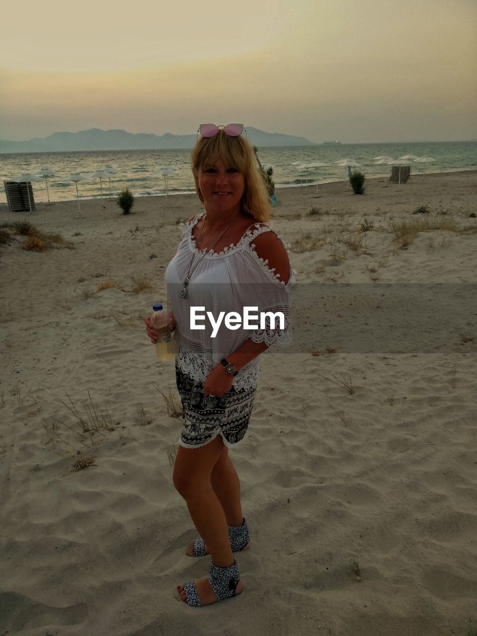 Portrait of mid adult woman standing on beach against sky during sunset