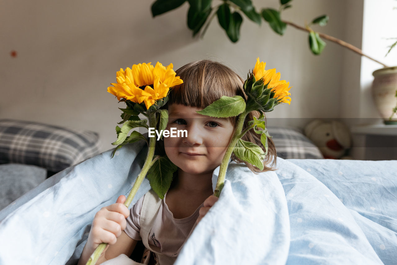 Portrait of a toddler girl holding sunflowers and looking at the camera