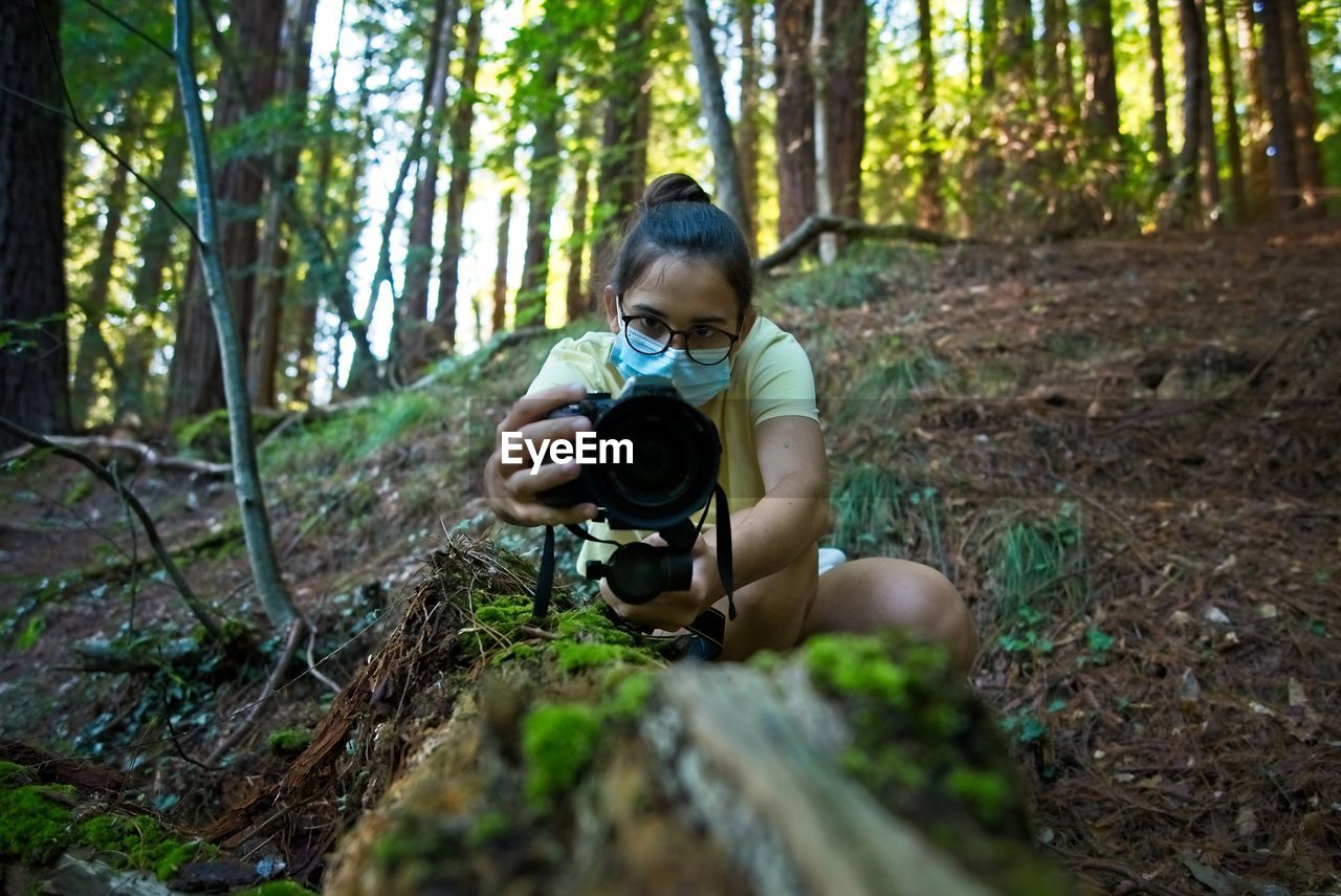 A teenage girl records a video on a fallen tree in the forest