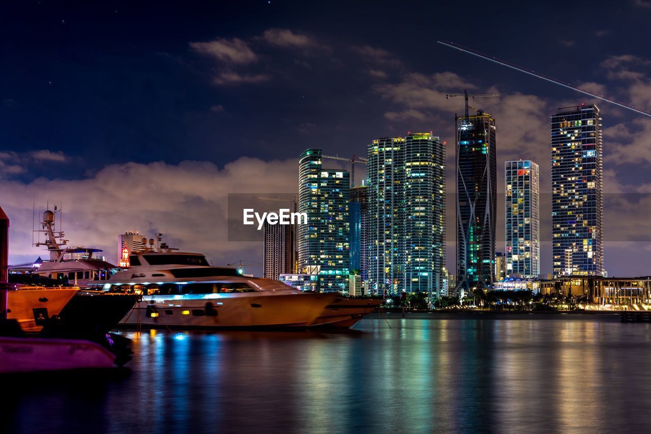 ILLUMINATED MODERN BUILDINGS BY SEA AGAINST SKY IN CITY