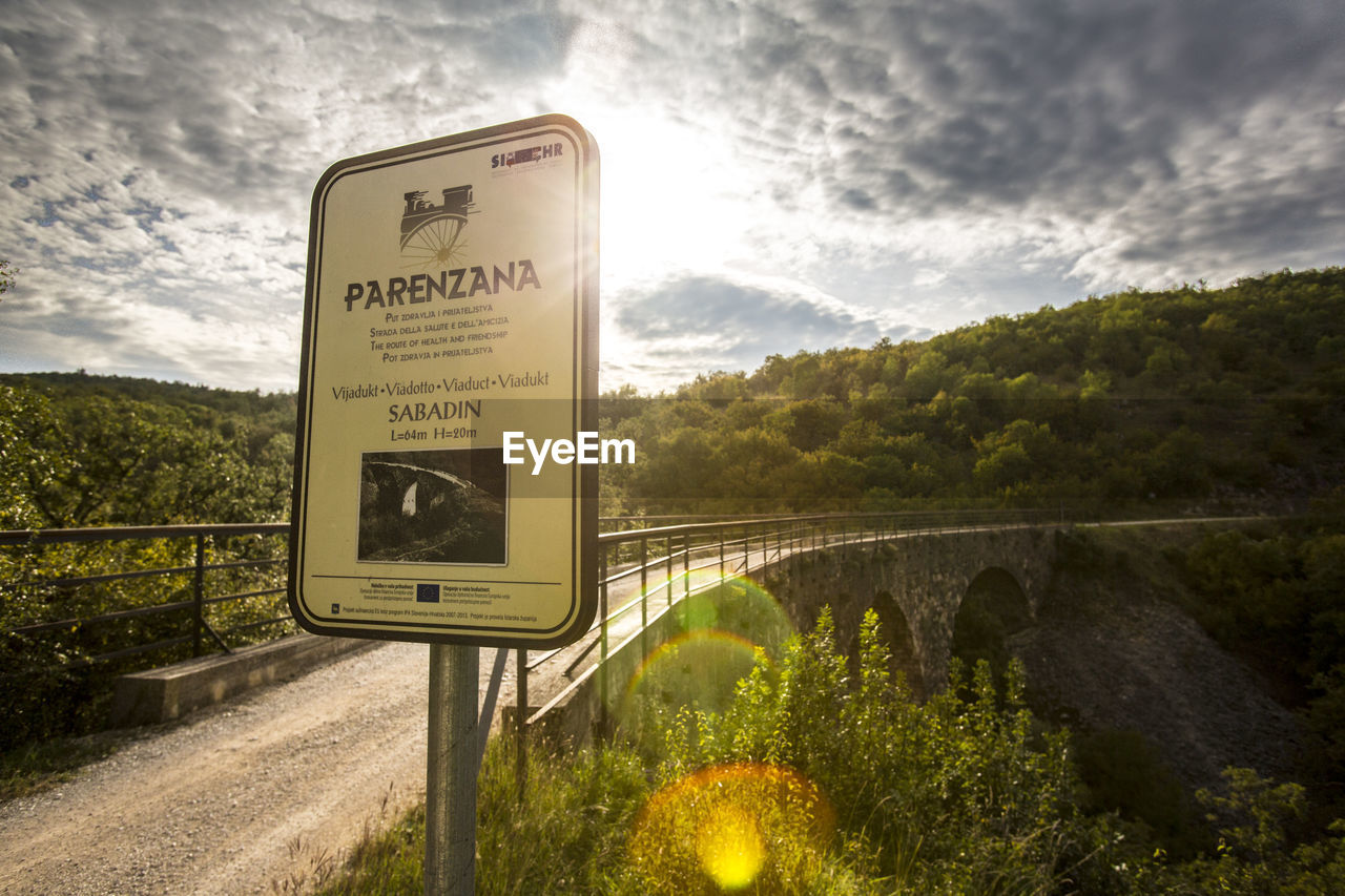 INFORMATION SIGN BY ROAD AGAINST TREES AND SKY